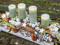Natürliche Adventsdeko: Kerzen in Salbeigrün mit Zapfen auf hellem Holz
