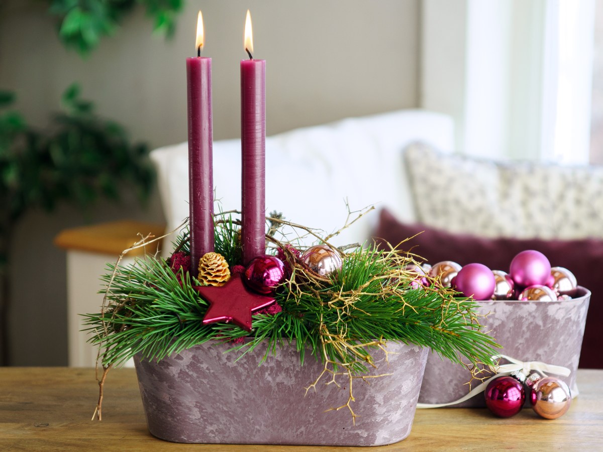 Adventsgesteck mit Kugeln in Beerentönen, daneben ein Topf voller rosa Weihnachtskugeln