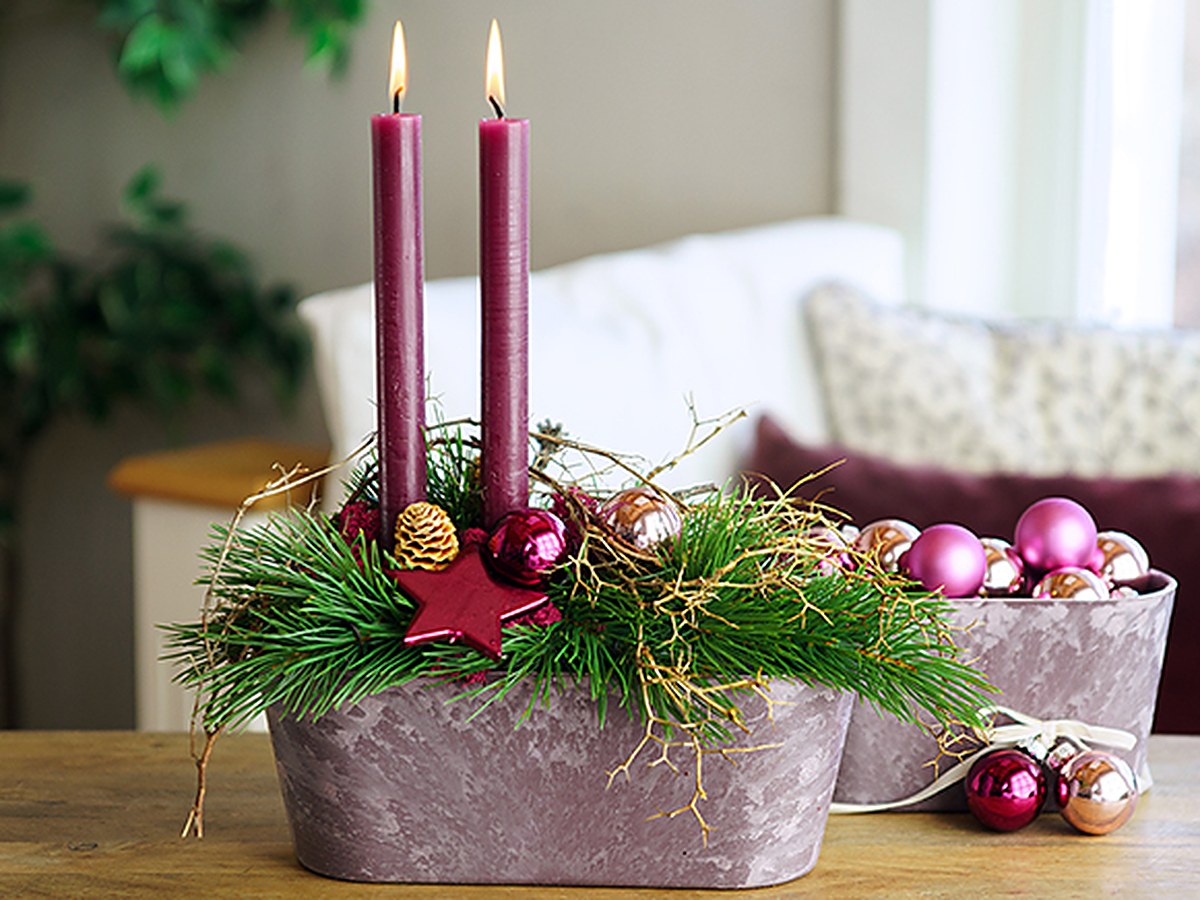 Adventsgesteck mit Kugeln in Beerentönen, daneben ein Topf voller rosa Weihnachtskugeln
