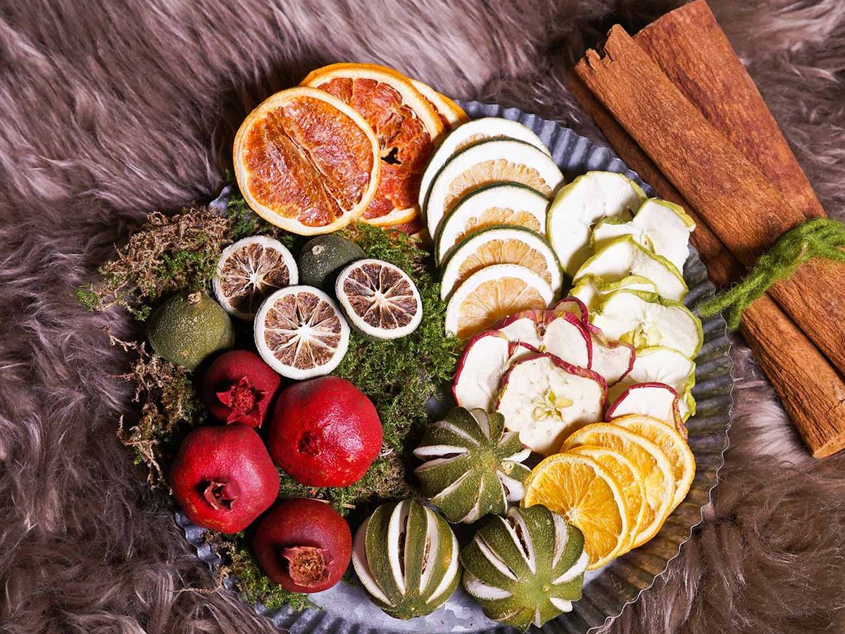 Getrocknete Orangenscheiben, Apfelscheiben, Limetten, Granatäpfel und Zimtstangen auf einem Zinkteller