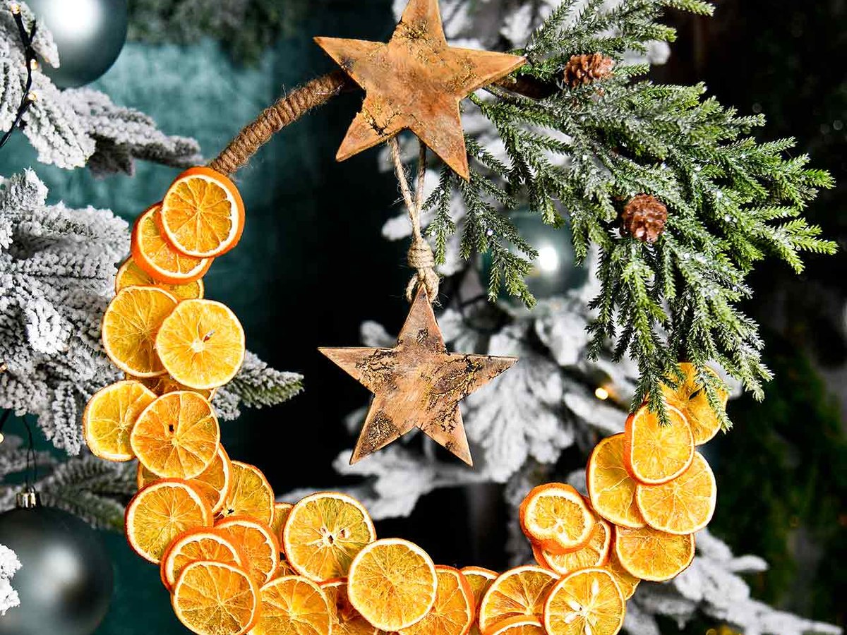 Kranz aus getrockneten Orangenscheiben mit Holzsternen und Tannenzweig an einem beschneiten Weihnachtsbaum