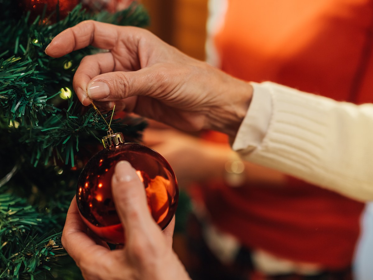 Hände hängen eine glänzende rote Weihnachtskugel an einen Tannenzweig