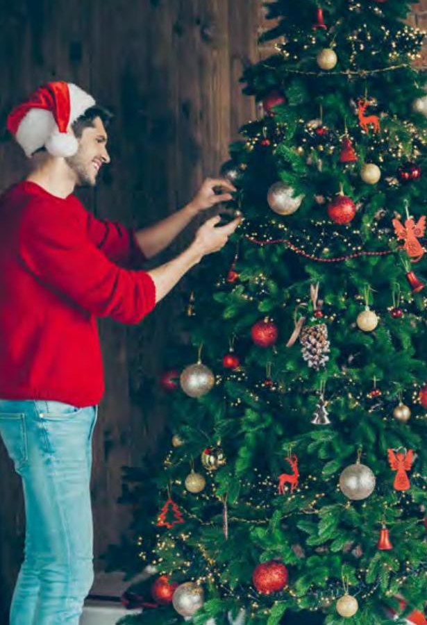 Mann schmückt einen Weihnachtsbaum mit roten und goldenen Weihnachtskugeln
