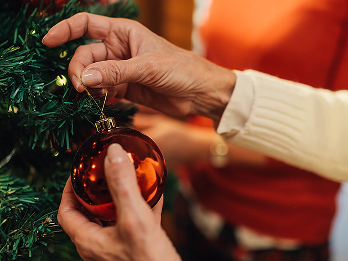 Hände hängen eine glänzende rote Weihnachtskugel an einen Tannenzweig