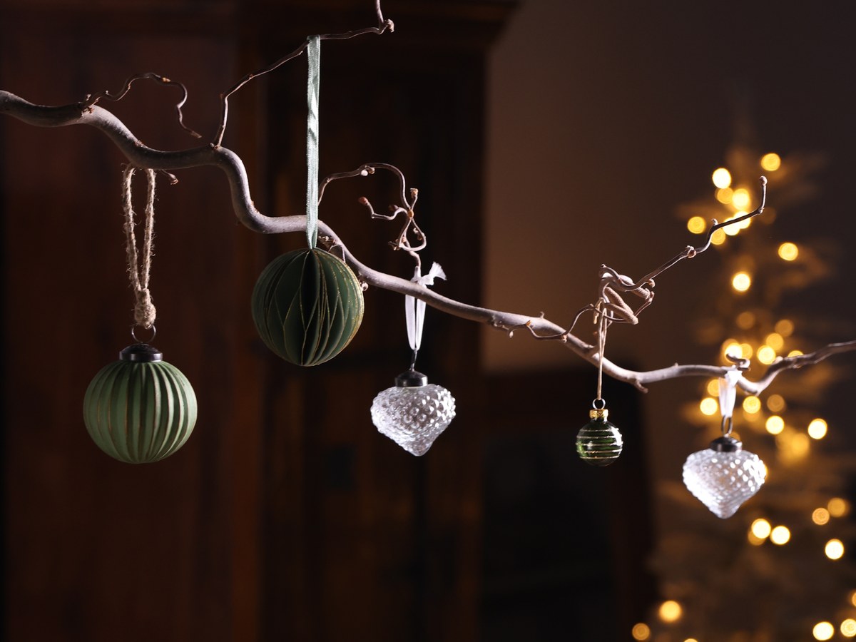 Grüne Weihnachtskugeln und Glasanhänger hängen an einem Zweig vor einer Lichterkette